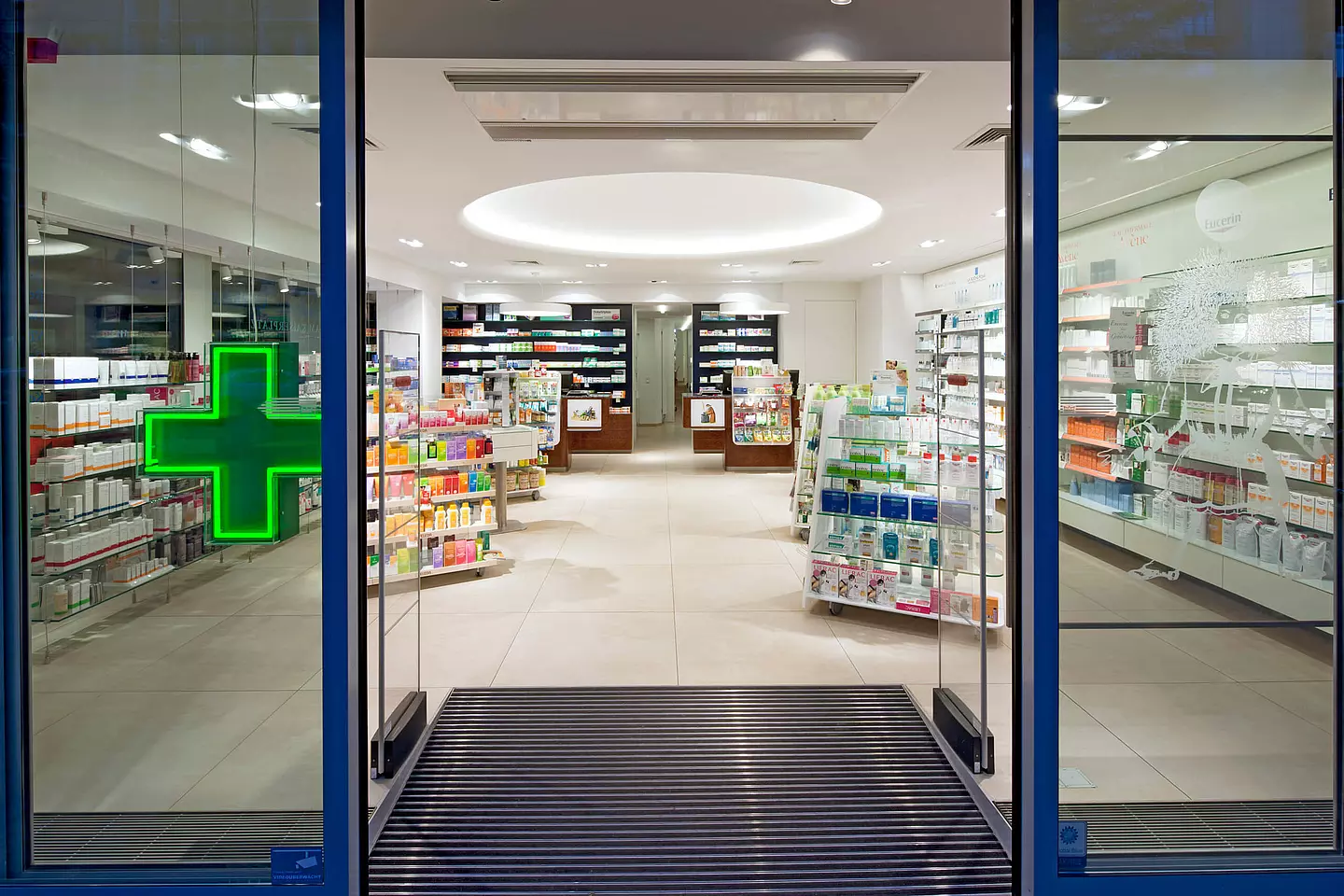 Außenansicht durch Fensterfront. Warensicherungskontrolle und leuchtendes Apothekenkreuz.
