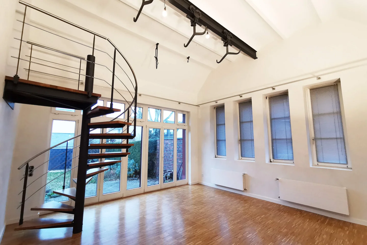 Lichtdurchflutetes Loft mit Kappendecke, Eichenparkett und skulpturaler Wendeltreppe. Historische Deckenstruktur trifft auf warme Materialien und klare, offene Raumwirkung.